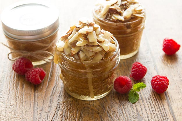 Honey almond cake in jars topped with almonds with raspberries and mint on a wooden surface.