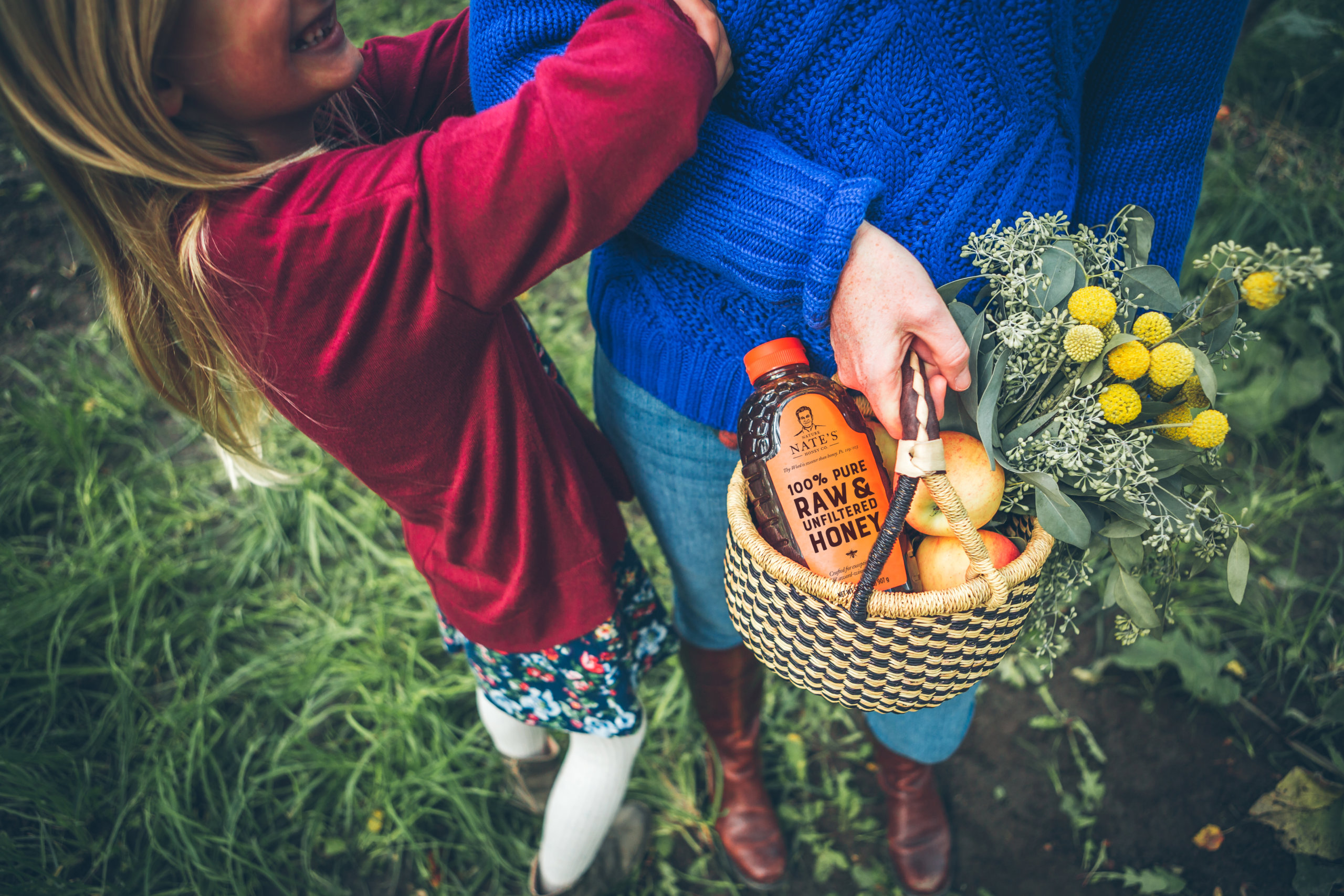 Child hugging adult holding a basket with honey and apples.