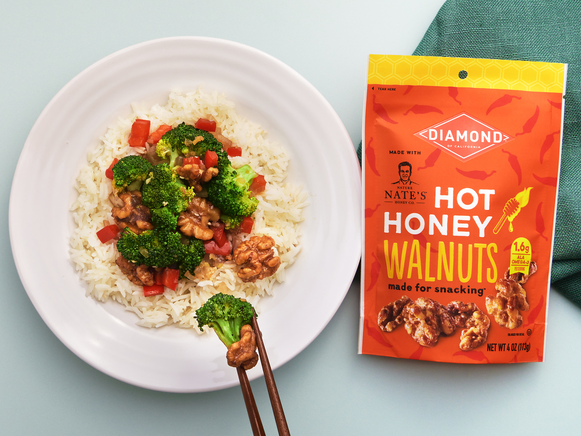 Broccoli and red pepper stir-fry over rice on a white plate with a package of Diamond hot honey walnuts.