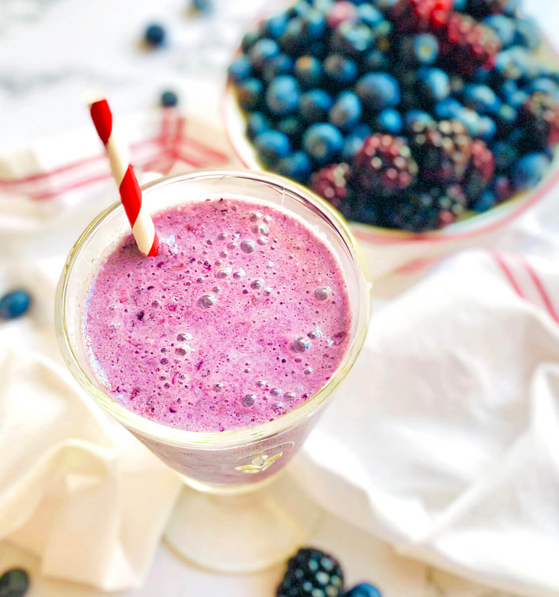 Berry smoothie with a straw, fresh berries in a bowl, on a striped napkin.