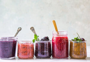 Row of colorful berry jams in glass jars, each with a spoon, against a soft backdrop. Row of colorful berry jams in glass jars, each with a spoon, against a soft backdrop.