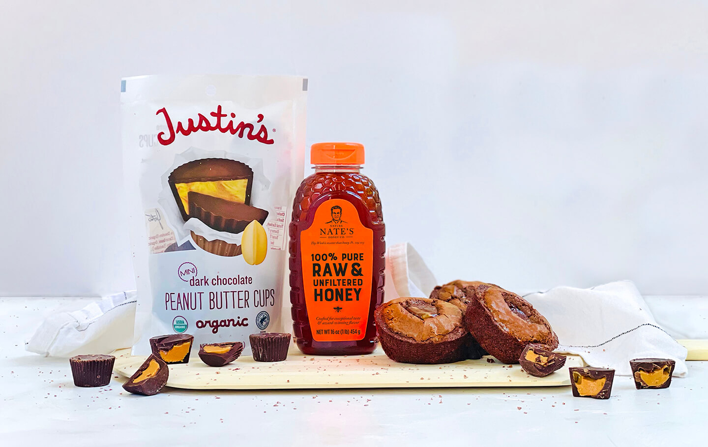 Bottle of Nate's honey with Justin's Peanut Butter Cups and treats on a white background.