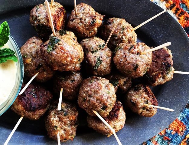 Skewered meatballs on a slate plate with dip, vibrant textile underneath.