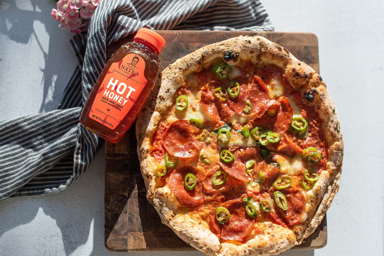 Pepperoni and jalapeno pizza with a bottle of Nate’s hot honey with a red cap on a wooden board.