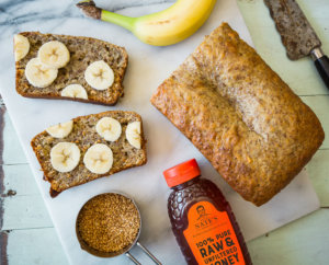Banana bread loaf with sliced pieces topped with banana slices next to bottle of Nate's honey.