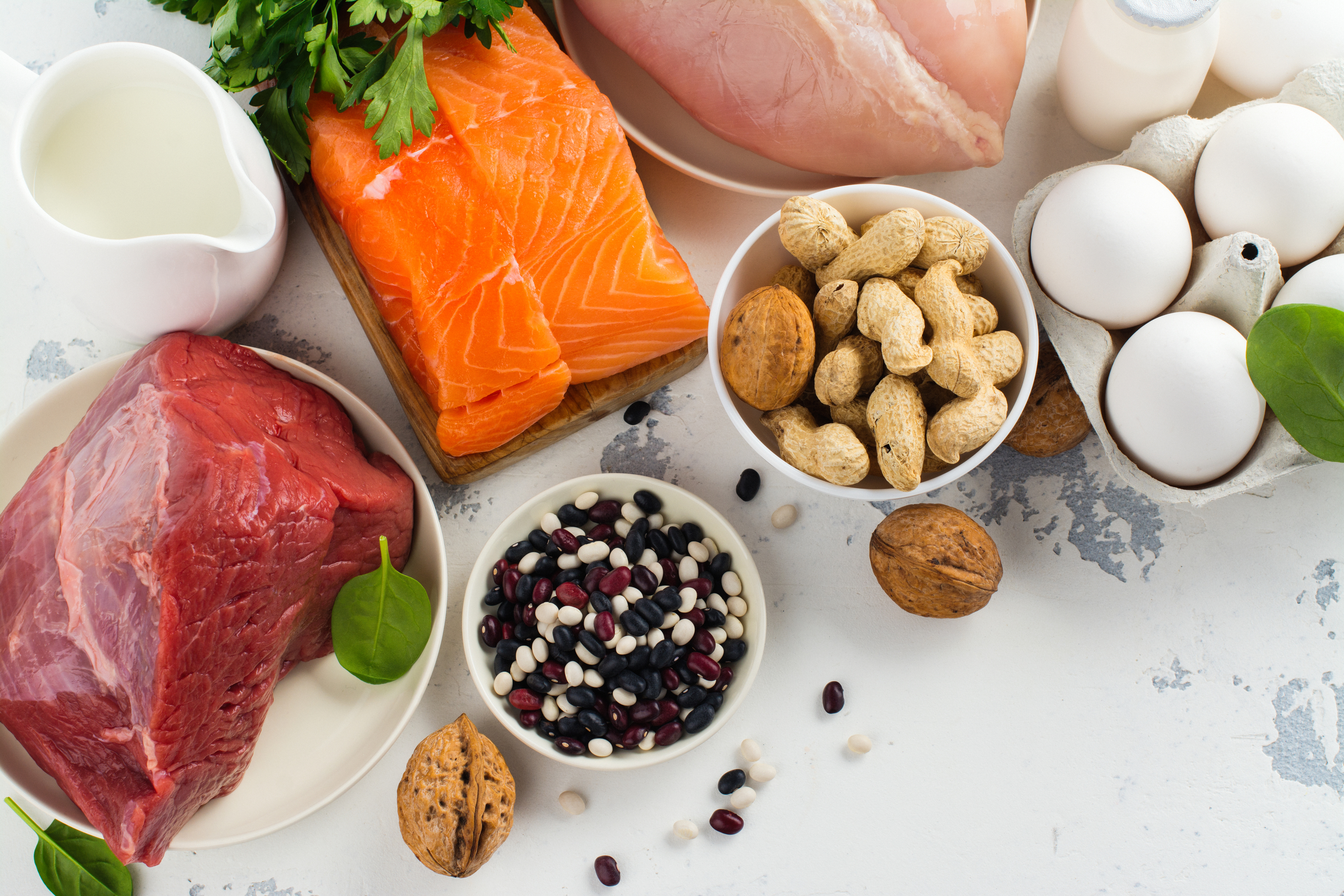 Assorted high-protein foods: meats, nuts, eggs, and milk on a light background.