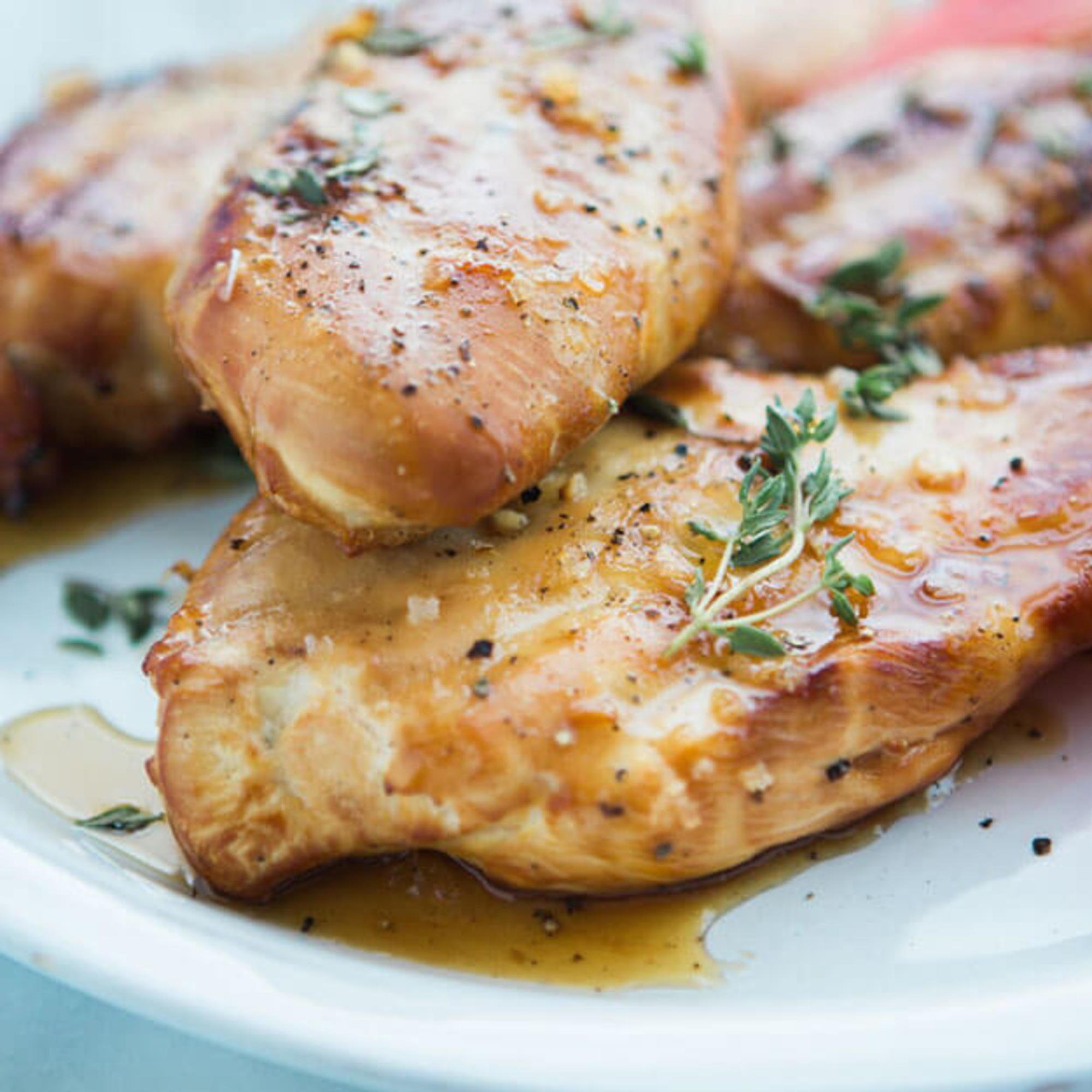 Grilled chicken breasts seasoned with herbs on a plate, showcasing a golden-brown sear and juicy appearance.