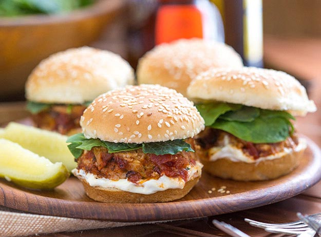 Meatloaf sliders with spinach on a wooden platter, pickles on the side.