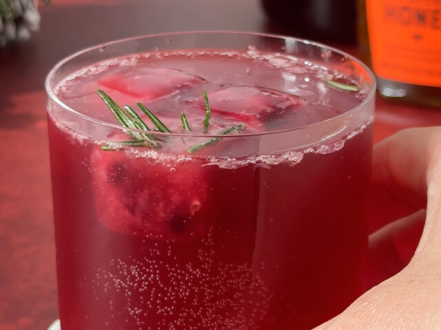 Cup filled with red Mistletoe Margarita Punch and rosemary, cranberry ice cubes.