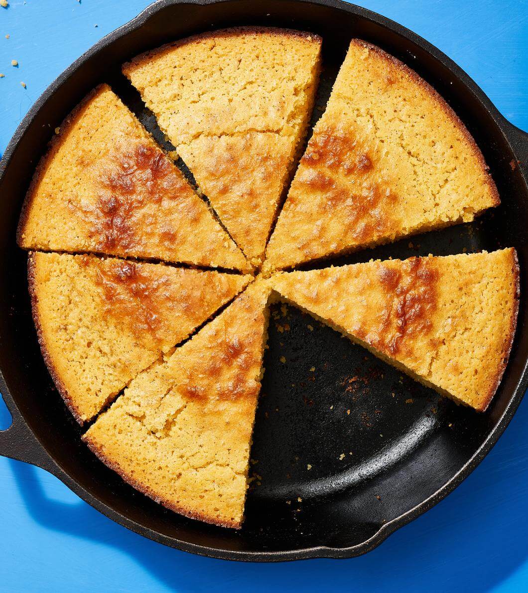 Sliced cornbread made with Nate’s honey in a skillet on a blue background.