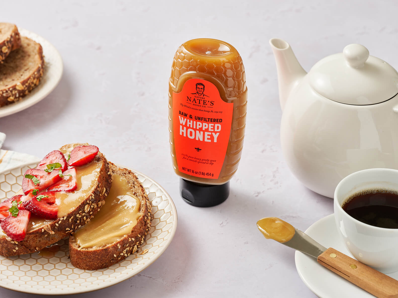 Bottle of Nate's whipped honey next to coffee, coffee pot and plate with toast