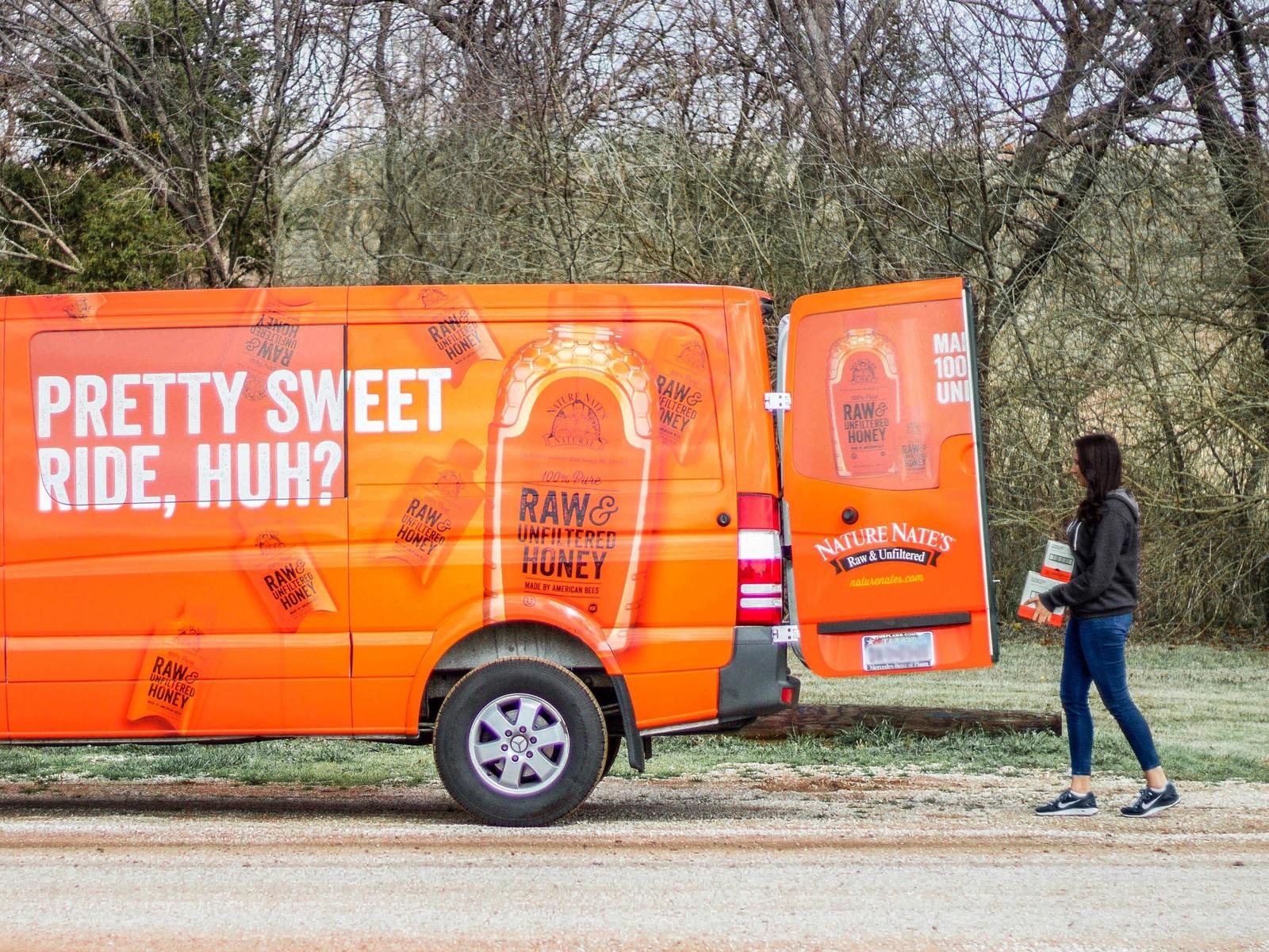 Person loading boxes into an orange delivery van with Nate's honey brand advertising.