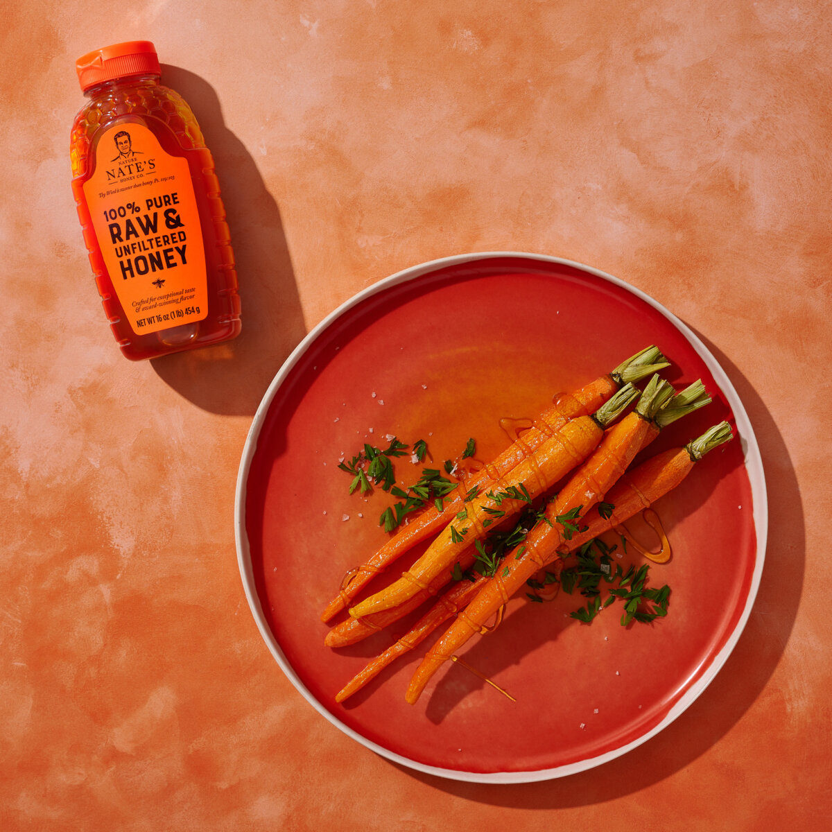 Honey-glazed carrots on a plate with Nate's honey bottle on the side on an orange background.