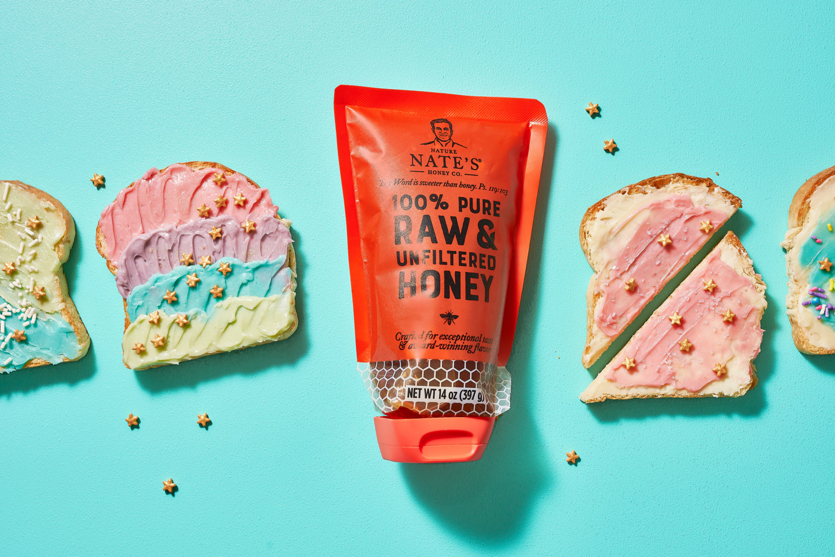 A tube of Nate's Raw & Unfiltered Honey next to slices of bread with colorful spreads on a blue background.
