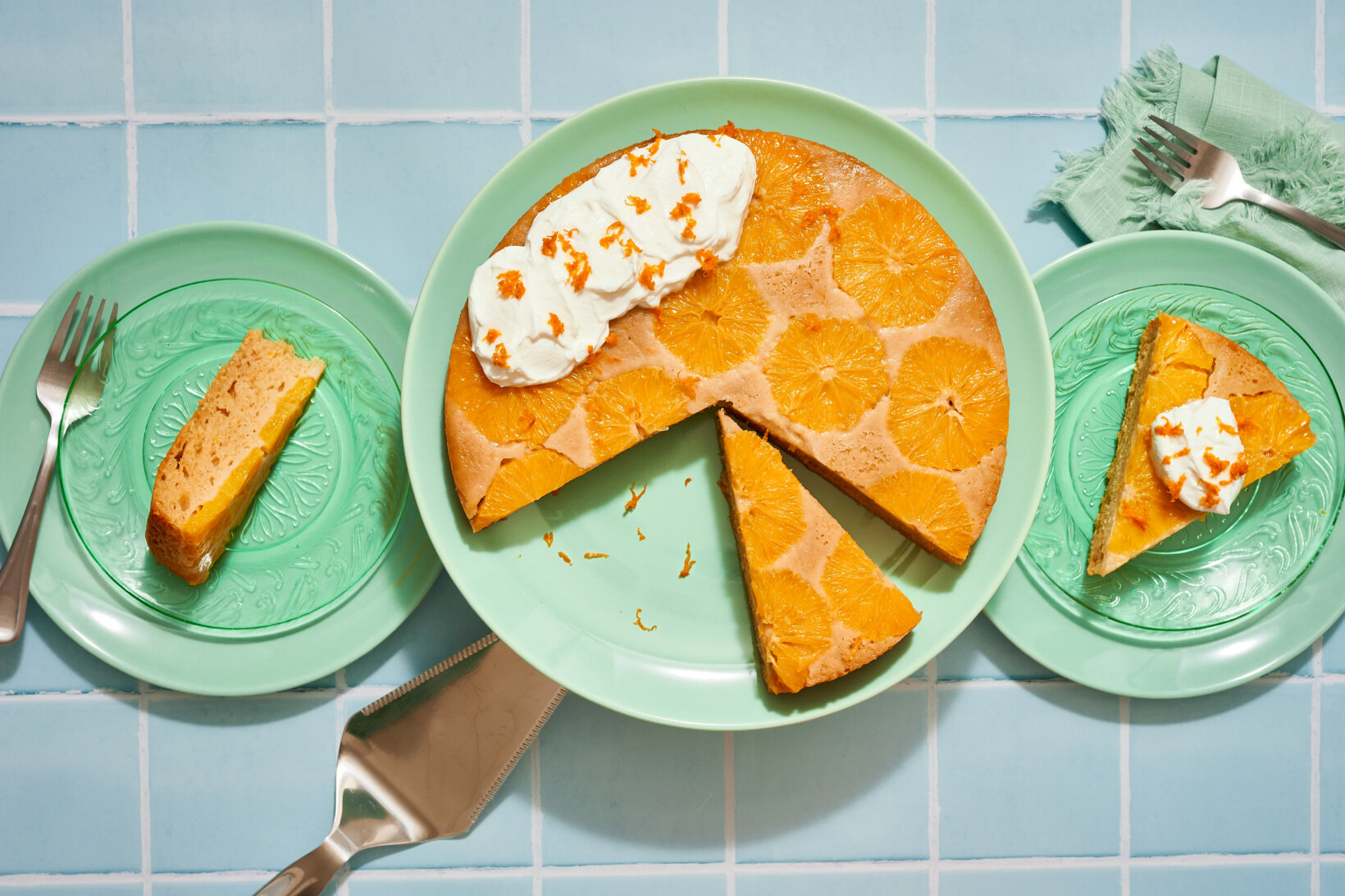 A sliced olive oil cake made with Nate’s honey with creamy topping served on green plates on a blue tiled table.