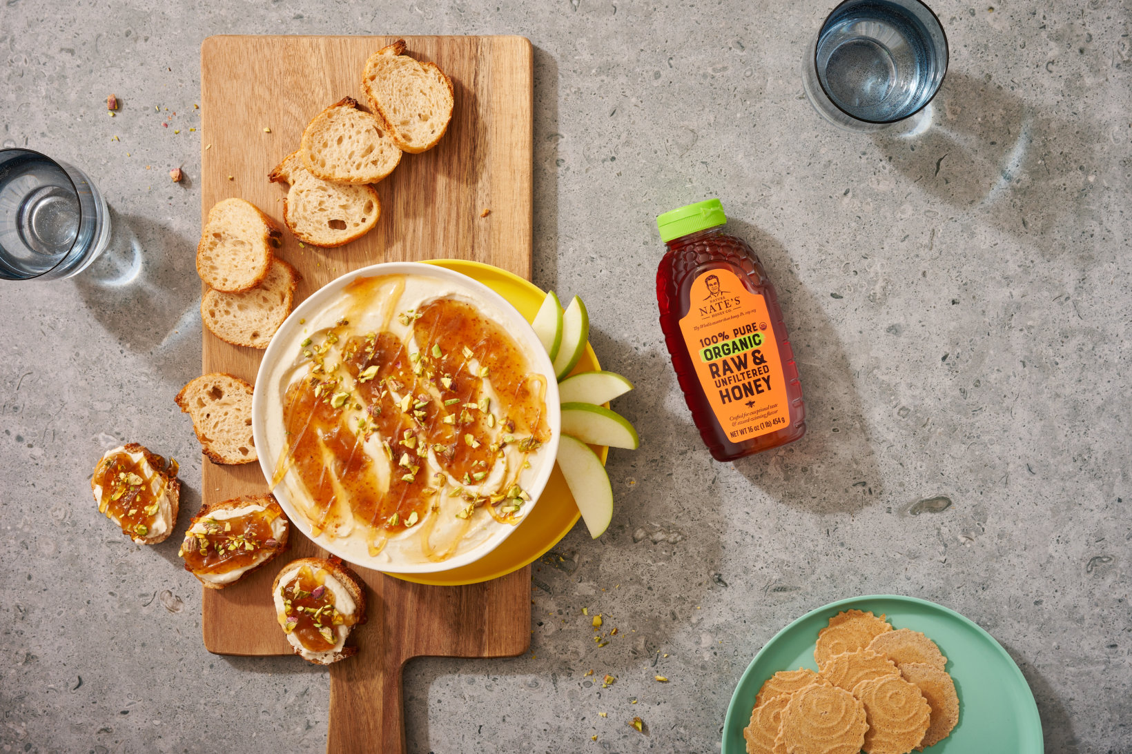 Cheese dip with honey and nuts, sliced apple, crostini, cookies, a bottle of Nate's organic honey and two glasses.