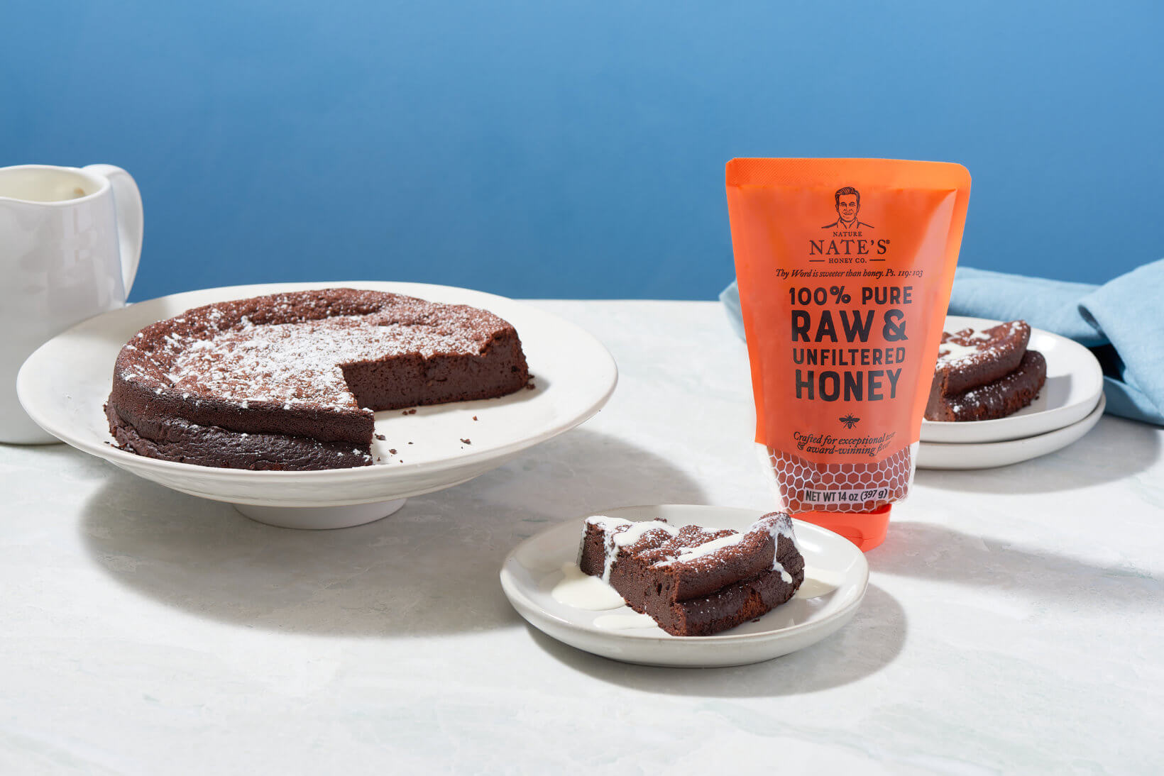 A chocolate cake dusted with powdered sugar next to a Nate's 100% pure raw & unfiltered honey pouch.