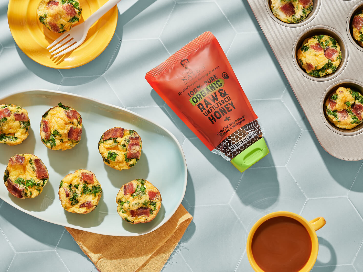 Egg bites made with bacon and honey on a tray with a Nate’s organic honey pouch and a cup of tea on a blue table.
