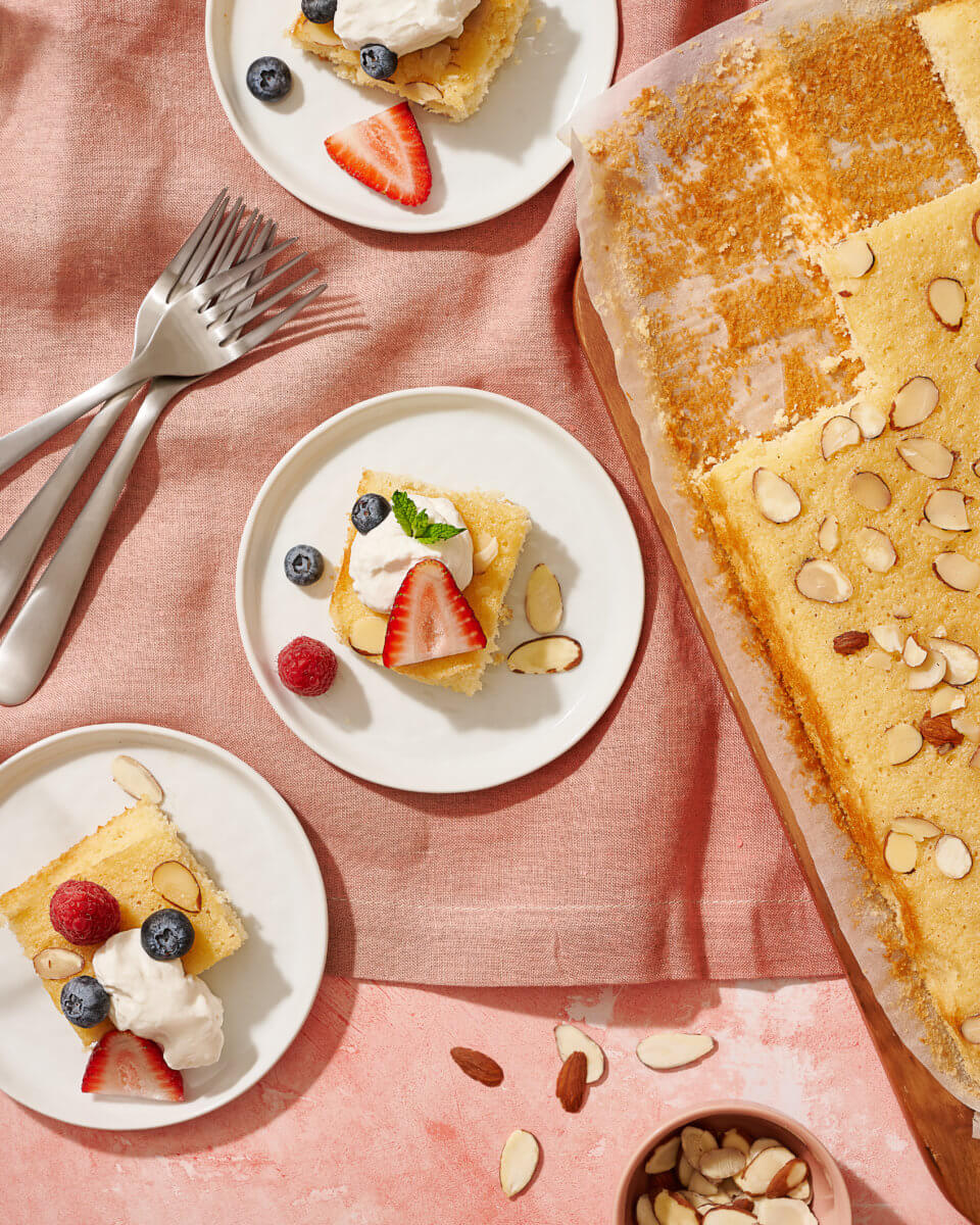 Slices of honey nut sheet cake topped with fresh berries served on small plates and three forks on pink cloth.
