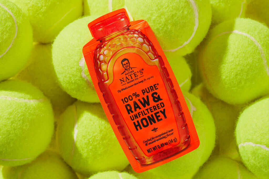 A Nate's honey mini sitting in a pile of green tennis balls.