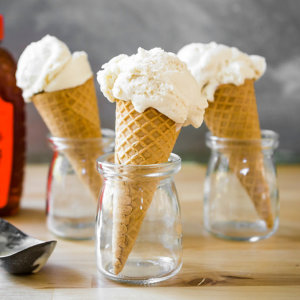 Vanilla ice cream cones in jars with honey bottle and scoop on a wooden table.