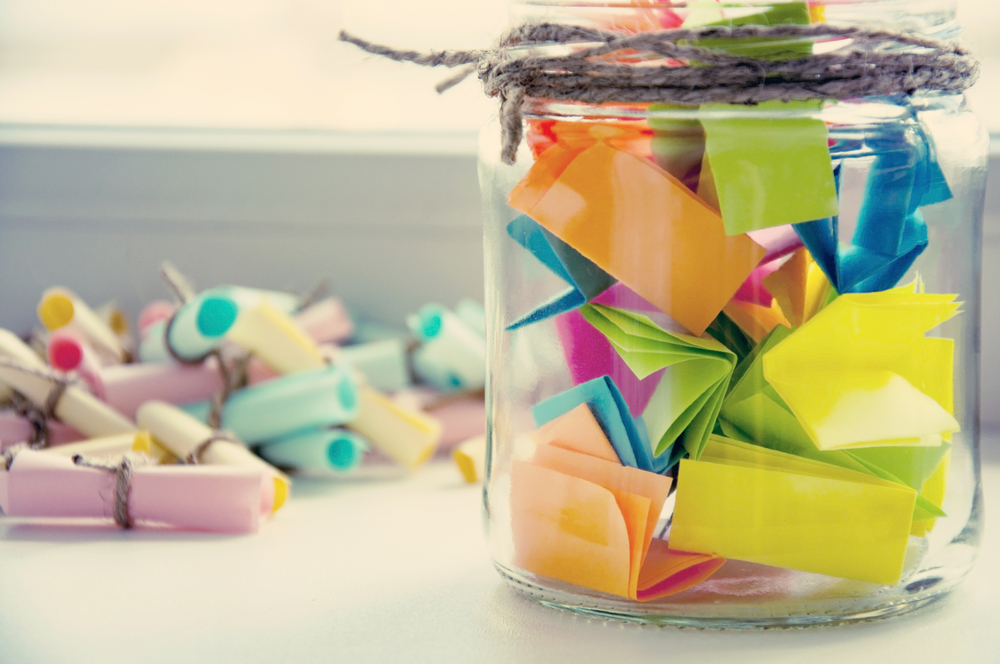 Jar filled with colorful paper notes and scrolls on a light background.