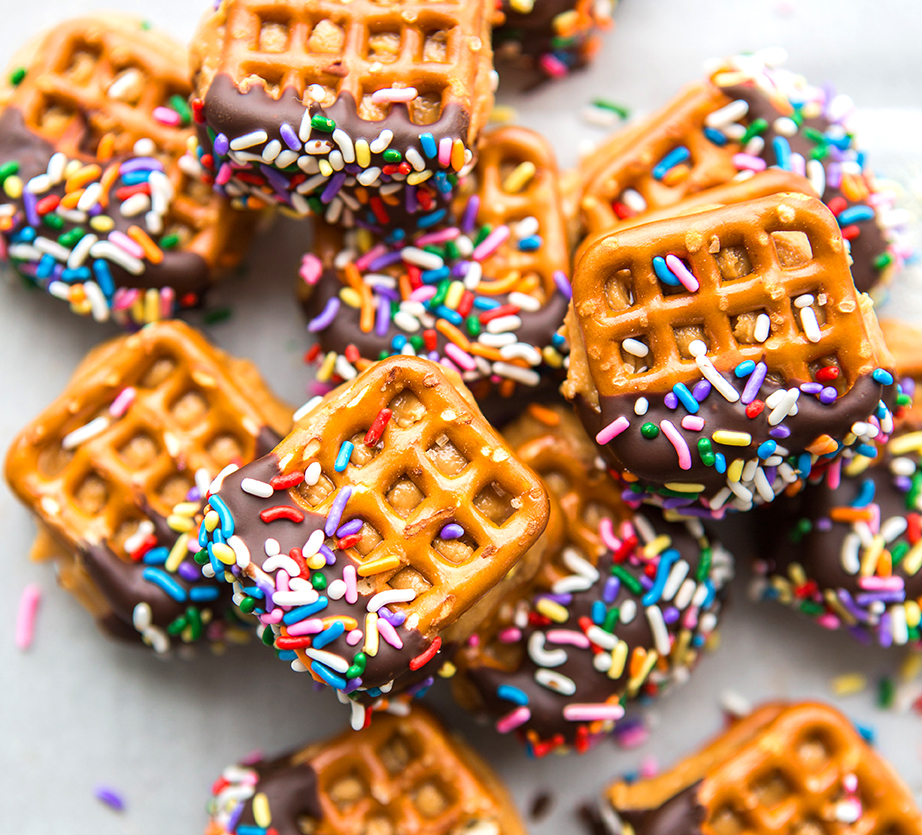 Chocolate-dipped pretzels with colorful sprinkles on parchment paper.