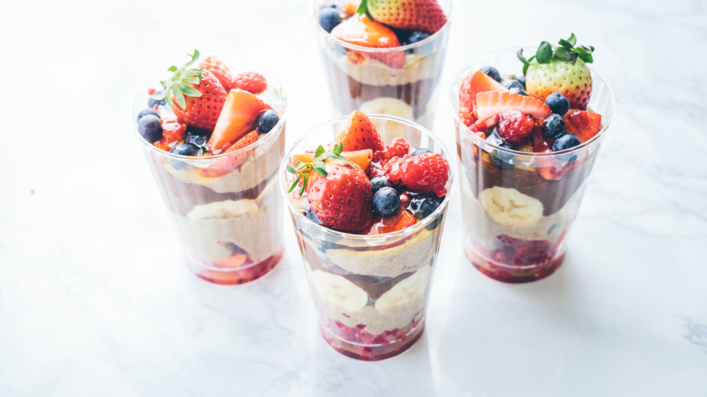 Four glasses of fruit parfaits with peanut butter, strawberries, blueberries and chocolate pudding on a marble counter.