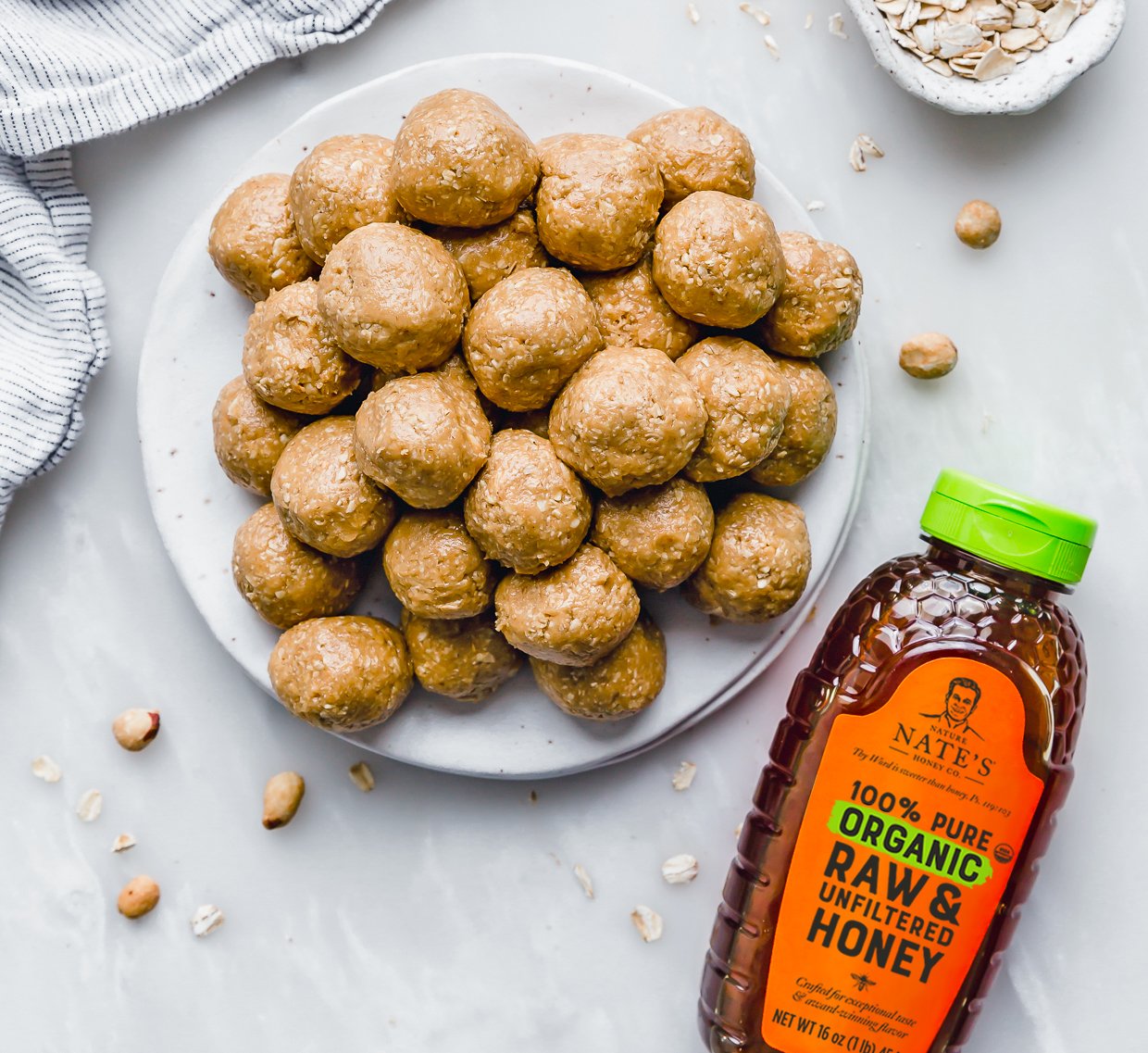 A plate of peanut butter cookie bites on a marble surface with a bottle of Nate’s organic honey and scattered peanuts.