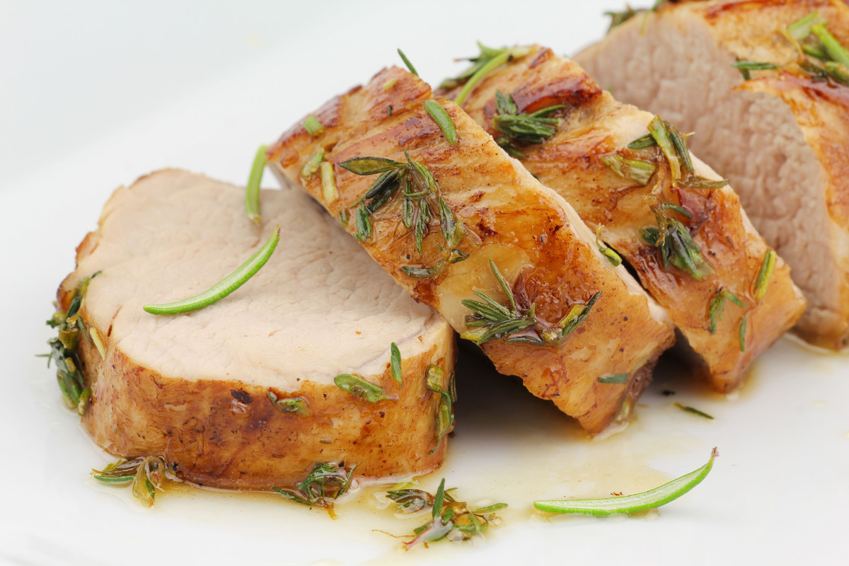 Sliced, herb-crusted pork loin on a white plate, garnished with fresh rosemary.