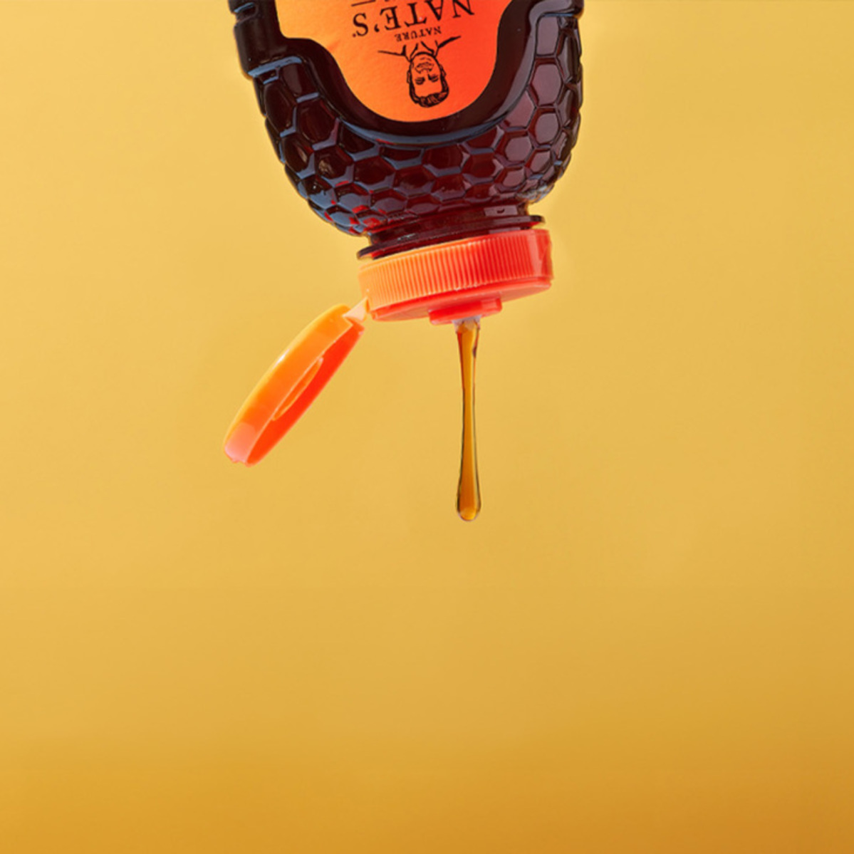 Upside-down honey bottle with honey dripping against a yellow background.