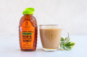 Nature Nate's organic honey bottle next to a cup of tea and fresh leaves on a white background. Nature Nate's organic honey bottle next to a cup of tea and fresh leaves on a white background.