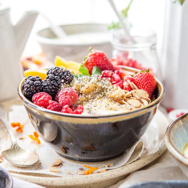 Smoothie bowl with mixed berries, nuts, and seeds, on a cloth with spoons.