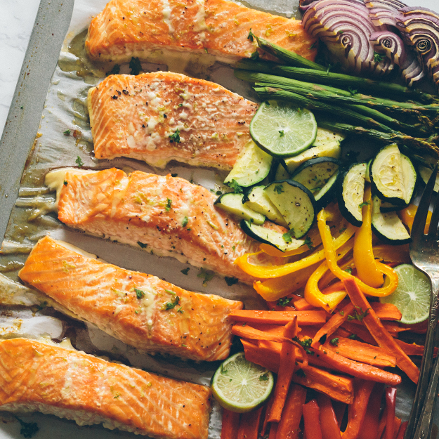 Baked salmon fillets and assorted colorful vegetables on parchment.