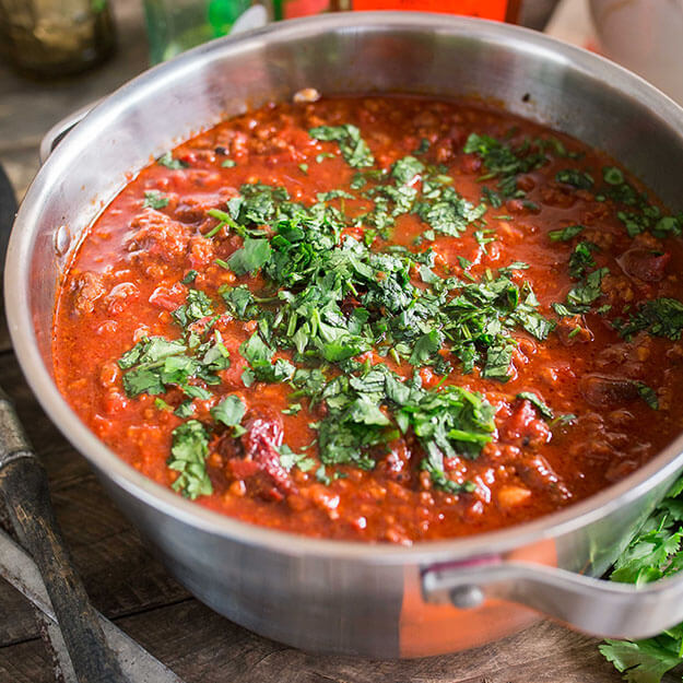 Chipotle bison chili garnished with fresh cilantro in a stainless-steel pot on a wooden surface.