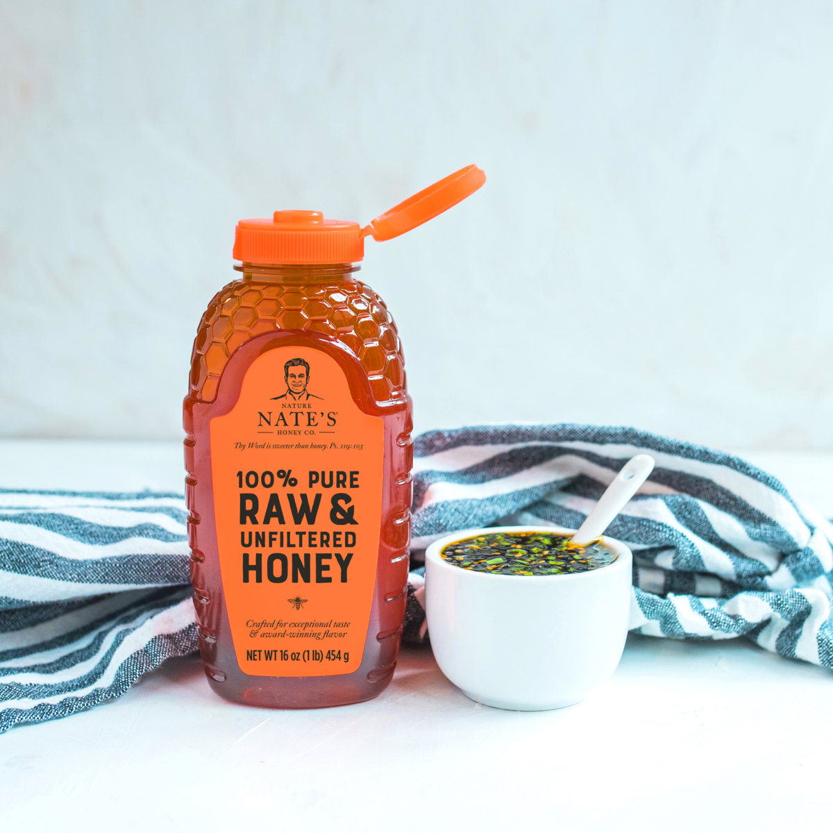 A bottle of Nate’s honey with an orange cap and a bowl with honey soy dipping sauce on a striped napkin.