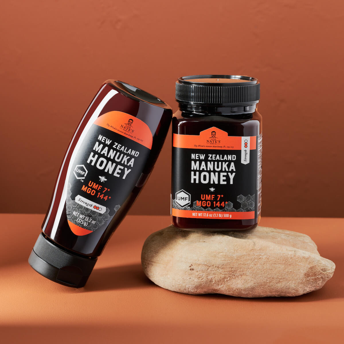 A bottle and jar of Nate’s manuka honey with UMF 10+ and UMF 7+ ratings, on a stone against a brown background.