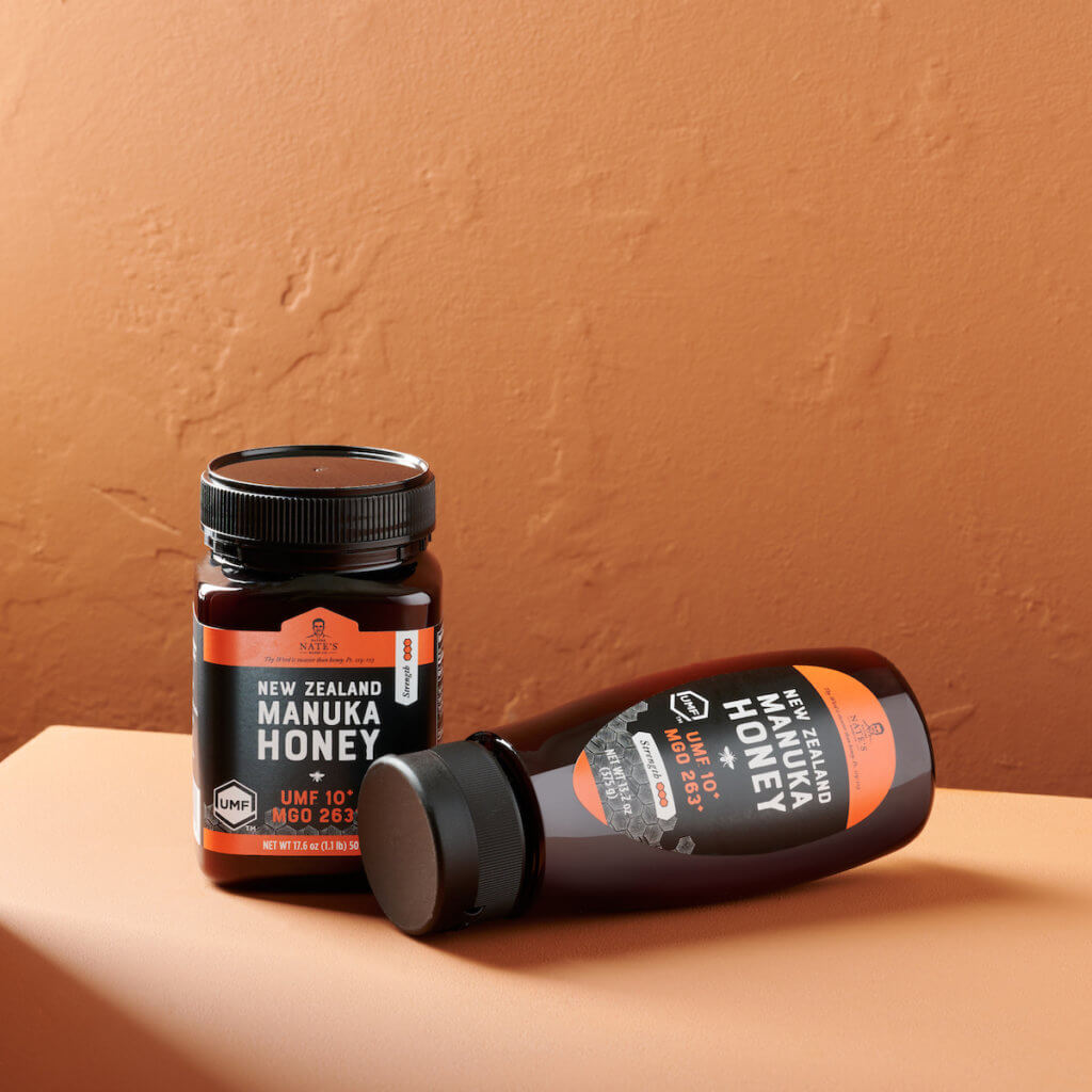 Two jars of Nate's New Zealand Manuka Honey on a peach-colored surface against a textured wall.