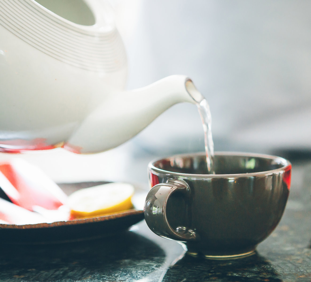 Teapot pouring hot water into a cup, with cookies on the side.