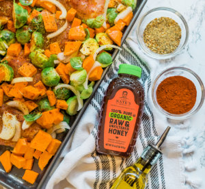 Roasted veggies with spices on a tray beside Nate's Honey, olive oil, and a checkered napkin.