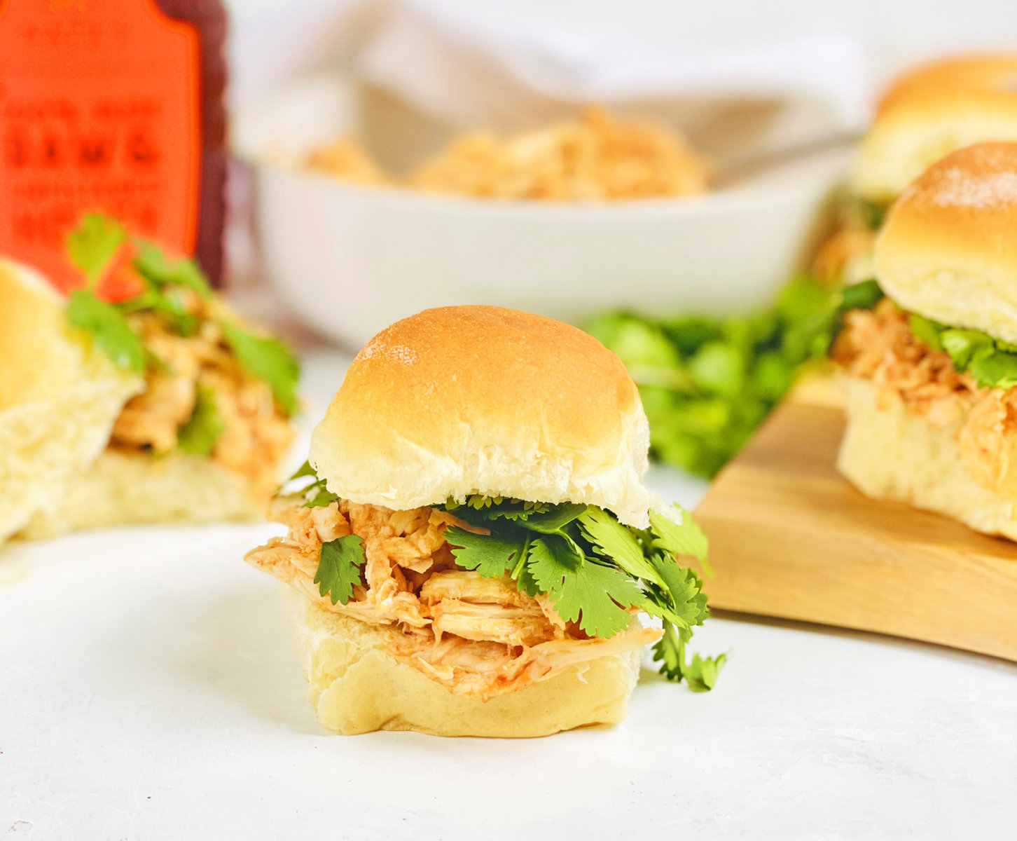 Chicken slider sandwiches with cilantro on a wooden board and a bottle of Nate’s honey in the background.