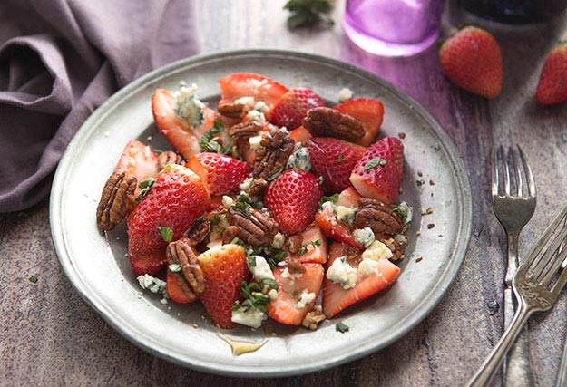 Strawberries with pecans and blue cheese on a speckled plate, with a fork on the side.