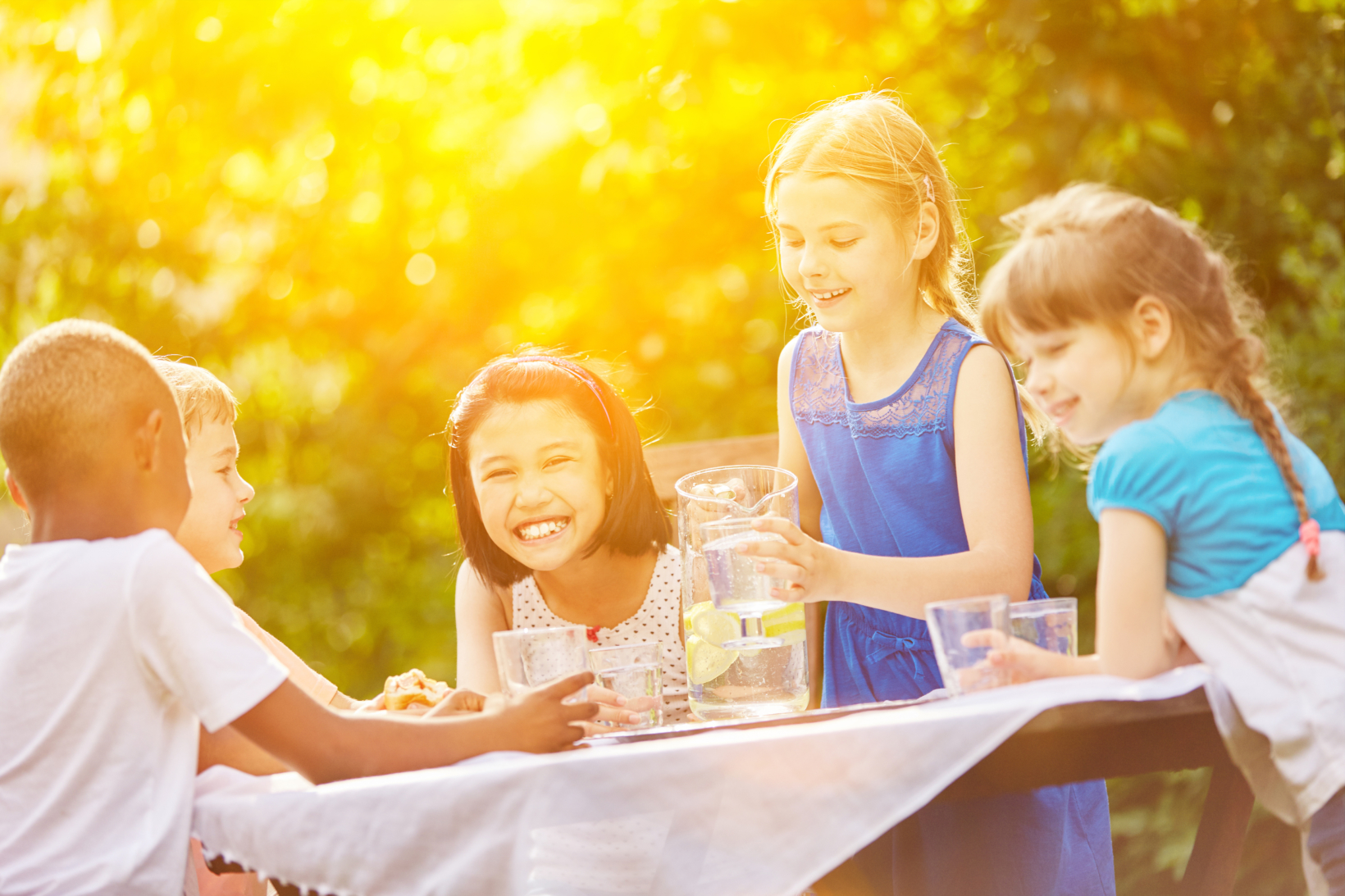 Children enjoying drinks and snacks outdoors in sunlight.