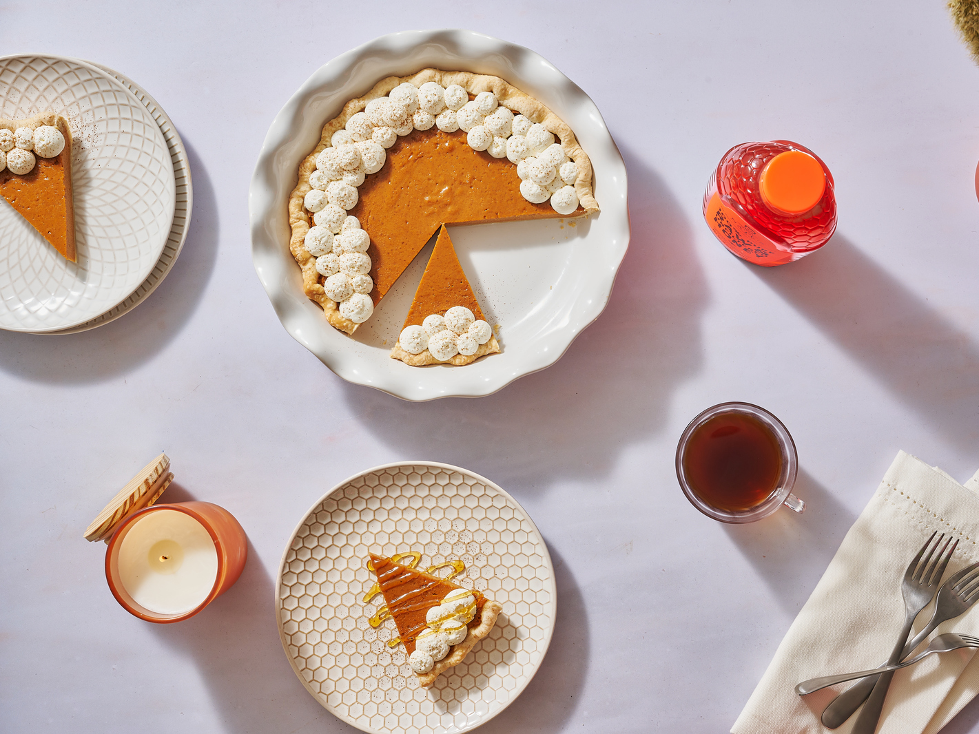 Sweet potato pie with whipped cream, a slice on a separate plate, coffee, a candle and bottle of Nate’s honey.