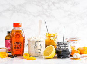 Vibrant Nate's honey bottle with homemade honey scrubs in jars on marble with citrus peels. Vibrant Nate's honey bottle with homemade honey scrubs in jars on marble with citrus peels.