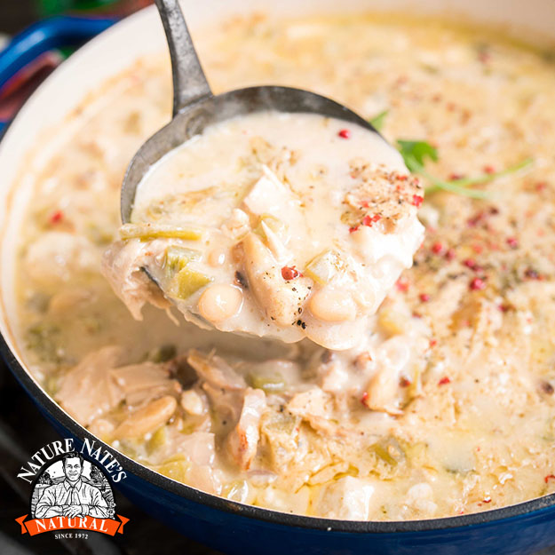 Creamy soup in a blue pot, ladle serving, topped with spices; logo of Nature Nate's in the corner.