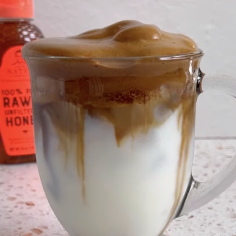Whipped coffee beverage in clear mug with Nate's honey bottle in background.