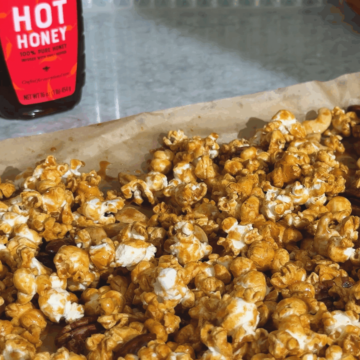 Caramel popcorn with nuts, made with hot honey, with Nate's hot honey in the background.