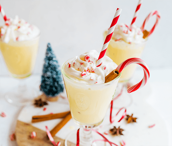 Festive eggnog in glasses with whipped cream, candy cane, and a holiday background.