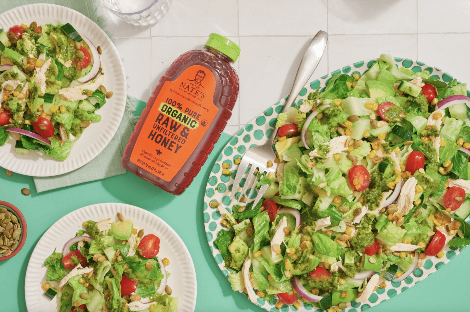 Fresh garden salads with avocado and cherry tomatoes, served next to a bottle of Nate’s organic honey with a green cap.